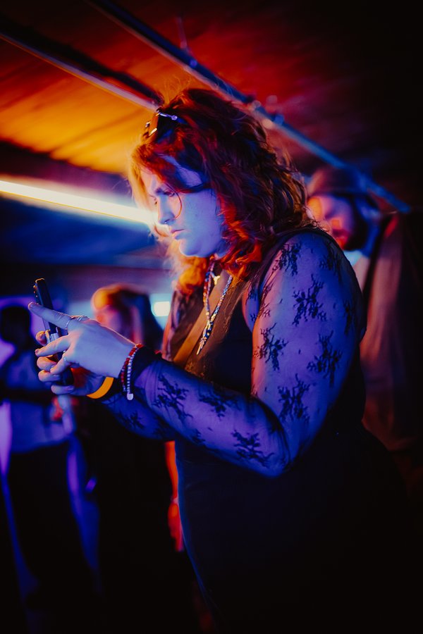 a raver on her phone under the neon at a black label radio show